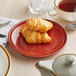 An Acopa Keystone Sedona Orange coupe plate with a croissant and a cup of tea on it.