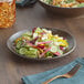 An Acopa Embers hickory brown matte coupe stoneware plate with a salad on a table.