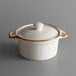 An Acopa Keystone white stoneware mini casserole dish with a brown rim and lid.