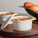 Two Acopa white stoneware mini casserole dishes with lids on a tray with soup and bread.