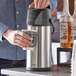 A man using an Acopa stainless steel airpot to pour coffee into a cup.