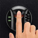 A finger pressing a button on a Barska black steel surface-mount biometric security safe with a keypad.