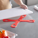 A person using a red Mercer Culinary cutting board grip on a cutting board.