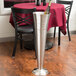 An American Metalcraft bucket stand with a wine bottle in it on a table with chairs.