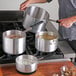 A man using a Choice aluminum sauce pan to cook soup on a stove.