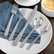 A white plate with Acopa stainless steel silverware on a blue cloth.