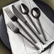 A black plate with Acopa Phoenix black stainless steel flatware on it.