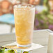 A stackable Choice plastic cooler glass filled with iced tea on a table.