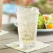 A Choice stackable plastic mixing glass filled with ice and soda on a table with a plate of salad.