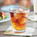A Choice plastic double rocks glass filled with ice tea on a table with ice tea and salad.