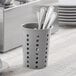 A gray perforated plastic flatware holder with utensils inside.