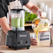 A man pouring orange juice into a black Galaxy commercial blender on a counter.