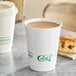 A white EcoChoice double wall paper hot cup filled with coffee next to a scone on a table.