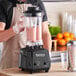 A person in an apron using a Galaxy commercial blender to make a smoothie.