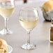 A table with two Acopa wine glasses of white wine next to a plate of bread.