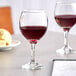 Two Acopa wine glasses on a table with a glass of red wine.