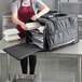 A woman in an apron using a Vesture Heavy-Duty Chafer Pan Carrier to put food in a white bag.