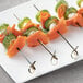A close-up of a skewer with salmon and cucumber on a white plate.