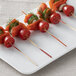 A white plate of sliced salmon and tomatoes on red bamboo skewers on a table.