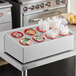A Choice stainless steel flatware organizer with red plastic cylinders holding utensils.