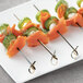 A close-up of a skewer of salmon and cucumber on a white plate.