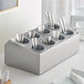 A stainless steel flatware organizer with gray plastic cylinders holding silverware.