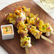 A bamboo skewer of chicken and cheese with a green bamboo paddle pick on a wooden board with sauce and green onions.