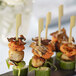 A black plate with a group of food skewered on green bamboo paddles.