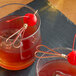 Two glasses of liquid with cherries on top held by red bamboo heart skewers.