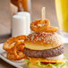 A burger with Bamboo by EcoChoice "Medium Well" Meat Marker on a plate with onion rings and a beer.