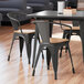 A Lancaster Table & Seating black metal arm chair with a natural wood seat on a wood floor.
