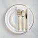 A white plastic plate with gold banded plastic flatware on it.