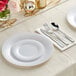 A white plastic dinner plate with hammered silver plastic flatware on a table with more settings.