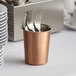 A Choice solid copper flatware holder cylinder filled with forks.
