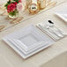 White plastic dinnerware and silver classic flatware on a table with flowers.