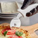A person holding a Choice pizza cutter with a white handle cutting a pizza.