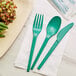 A green EcoChoice CPLA fork, spoon, and knife on a napkin.