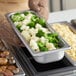 A person holding a Vigor stainless steel steam table pan filled with broccoli and cauliflower.