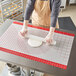 A person rolling Fat Daddio's silicone baking work mat on a table.