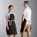 A man and woman wearing black Choice bib aprons with natural webbing accents.