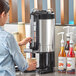 A woman using an Estella Caffe thermal coffee server to pour coffee from a bottle into a coffee machine.