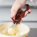 A hand using a brown Vollrath Jacob's Pride #70 squeeze handle to scoop butter.