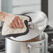A hand using a white towel to clean a pot lid.