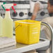 A yellow Noble King-Pail 3 quart cleaning pail on a cleaning cart next to spray bottles and cleaning cloths.