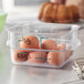 A Carlisle clear square food storage container filled with brown eggs with writing on the shells.