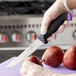 A gloved hand with a black and purple Schraf utility knife cutting a pear.