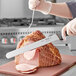 A person slicing a large piece of ham with a Schraf serrated knife.