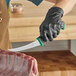 A person in black gloves using a Schraf curved boning knife to cut meat.