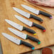 A group of Schraf chef knives with different colored TPRgrip handles on a cutting board.