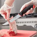 A person in gloves holding a Schraf utility knife with a red handle over a piece of meat on a counter.